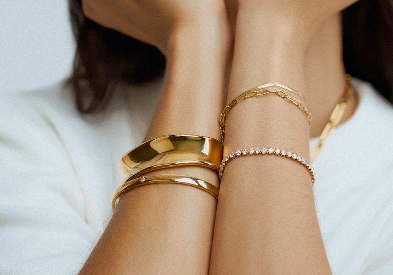 Orelia Jewellery bracelet stack. Model wearing a mix of gold bracelets, from bangles to tennis bracelet chains.