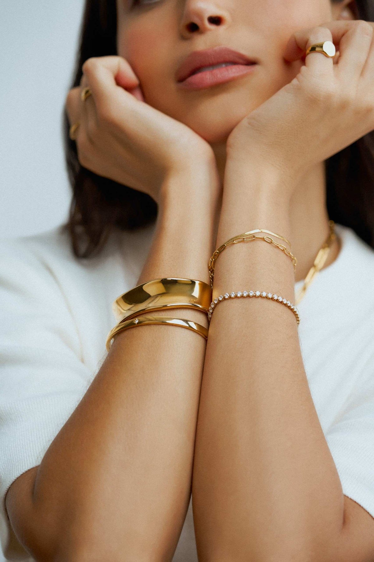 Orelia Jewellery bracelet stack. Model wearing a mix of gold bracelets, from bangles to tennis bracelet chains.